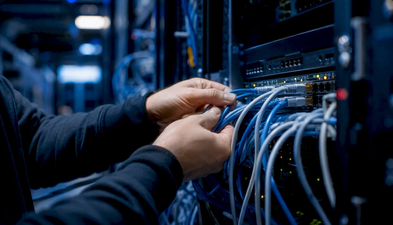 Hands plugging network cables in server rack